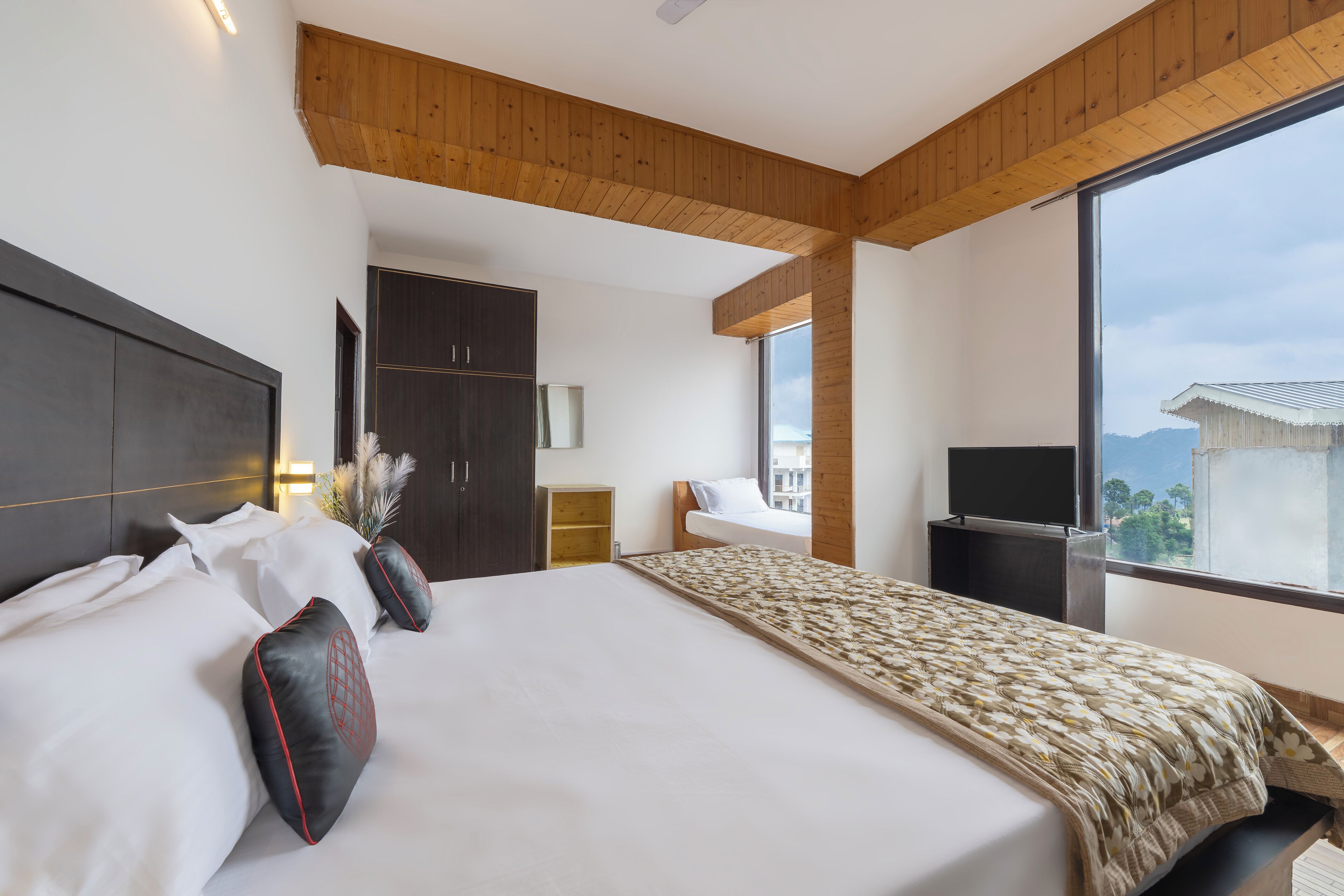 A modern hotel room with a large bed, wooden ceiling beams, a TV, and a view of the city.