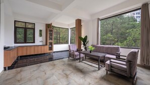 A modern living room with a sofa, chairs, a coffee table, and a kitchen area with a counter and cabinets. - The Chalet Homestay (Kasauli)
