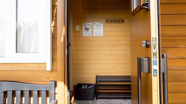 A wooden cabin with a bench outside, a door leading to a room with a bed and a small table, and a sign on the wall. - LAKE TOYA PREMIUM CABIN (Toyako)