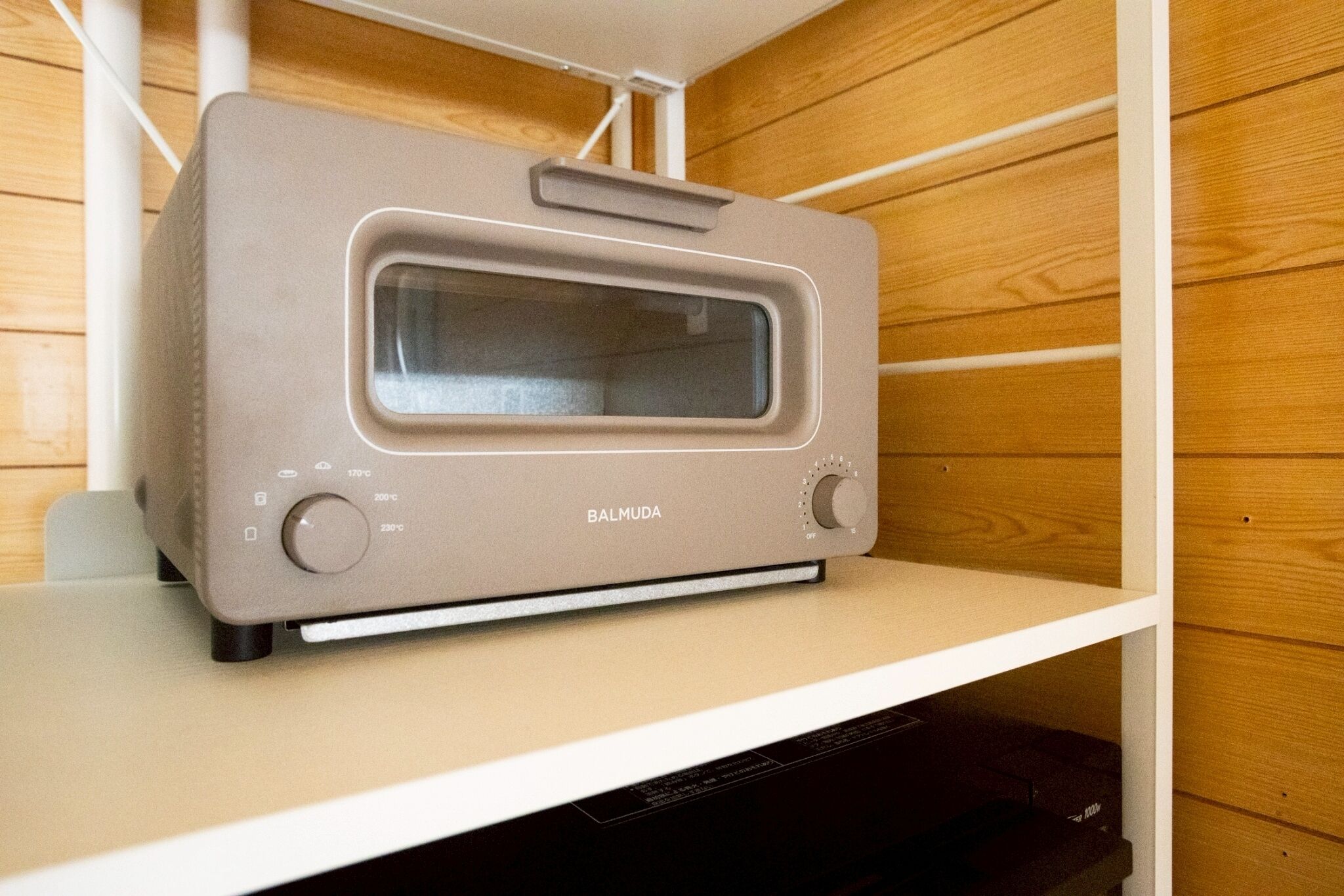 A beige toaster oven on a white shelf in a wooden-paneled kitchen.
