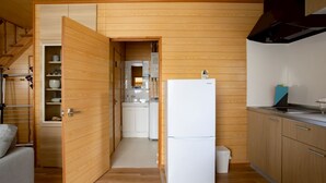A compact kitchen with wooden walls, a white refrigerator, and a small dining area. - LAKE TOYA PREMIUM CABIN (Toyako)