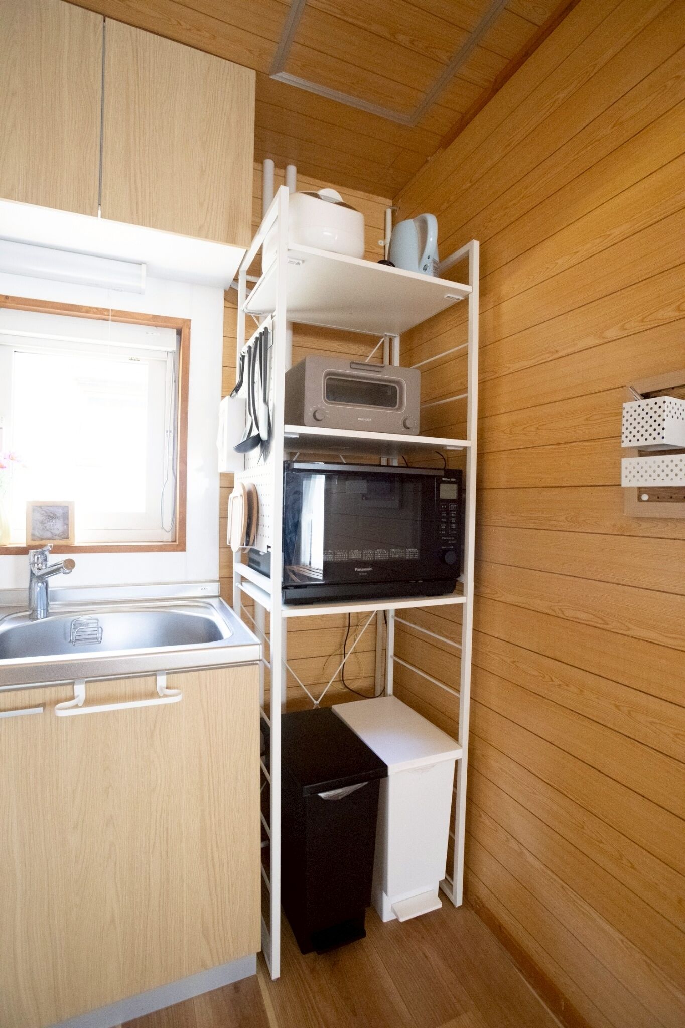 Una cucina compatta con lavello, mobili bianchi e un forno a microonde su uno scaffale bianco.