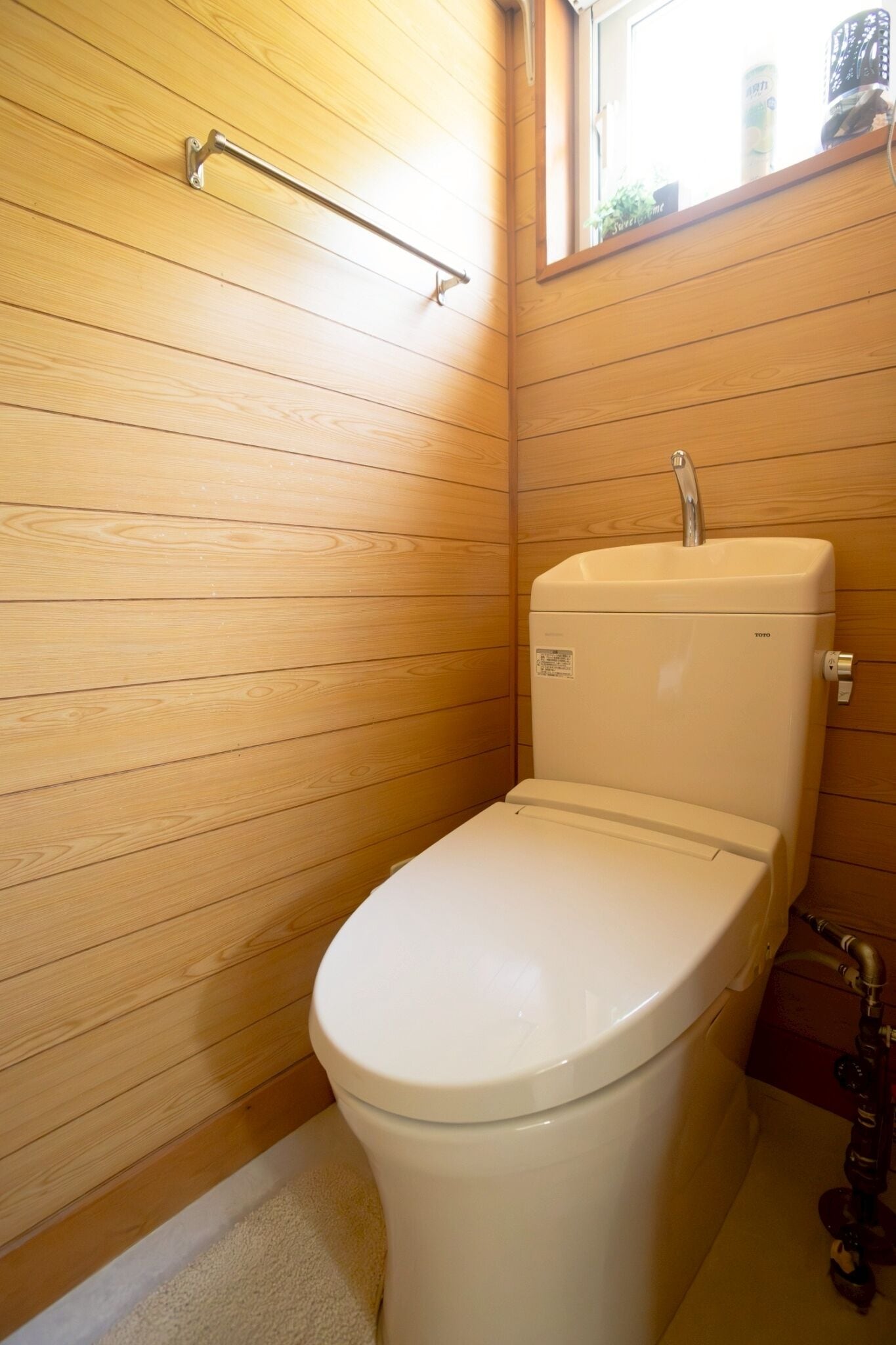 A small, compact bathroom with wooden panel walls, a white toilet, and a window above the sink.