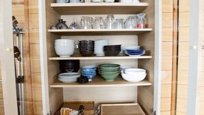 A wooden cabinet with shelves containing various kitchenware and a basket with utensils. - LAKE TOYA PREMIUM CABIN (Toyako)