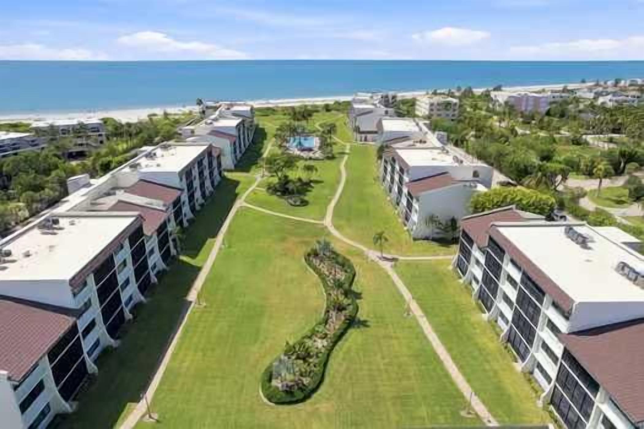 A hotel with multiple buildings, a central lawn, and a view of the ocean.
