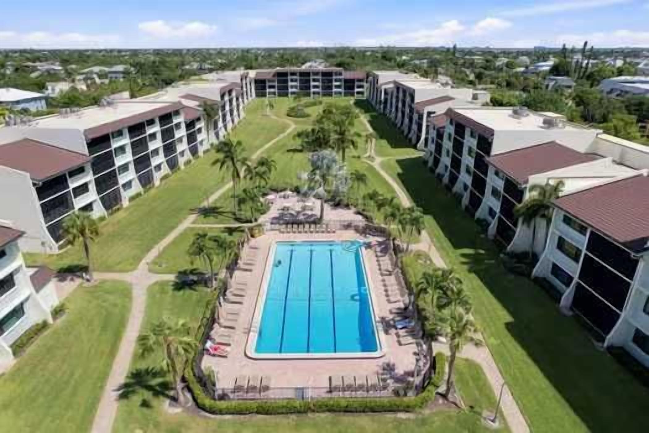 A hotel with a central swimming pool, multiple floors, and a surrounding lawn.