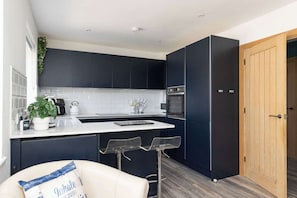 Une cuisine moderne avec des meubles de couleur sombre, un plan de travail blanc et une porte en bois.