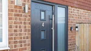 A modern door with a number '4' and a glass panel, set in a brick wall with a wooden fence nearby. - Coastal Retreat with Hot Tub, Walk to Beach (West Wittering)
