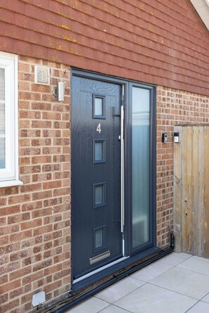 A modern door with a number '4' and a glass panel, set in a brick wall with a wooden fence nearby.