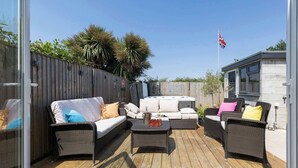 An outdoor patio with wicker furniture, a hot tub, and a flag. - Coastal Retreat with Hot Tub, Walk to Beach (West Wittering)