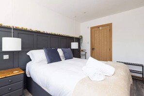 Ein ordentlich bezogenes Bett mit weißer und blauer Bettwäsche, ein Nachttisch aus Holz, eine Hängelampe und eine Holztür.