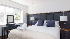 Un lit bien fait, recouvert d’une couette blanche, une table de chevet avec une lampe, et une fenêtre donnant sur un paysage verdoyant.