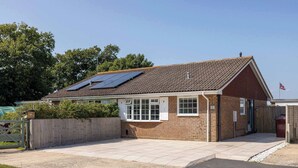 Un bâtiment d’un seul étage, construit en briques, avec un toit recouvert de tuiles, des panneaux solaires et un petit garage attenant.