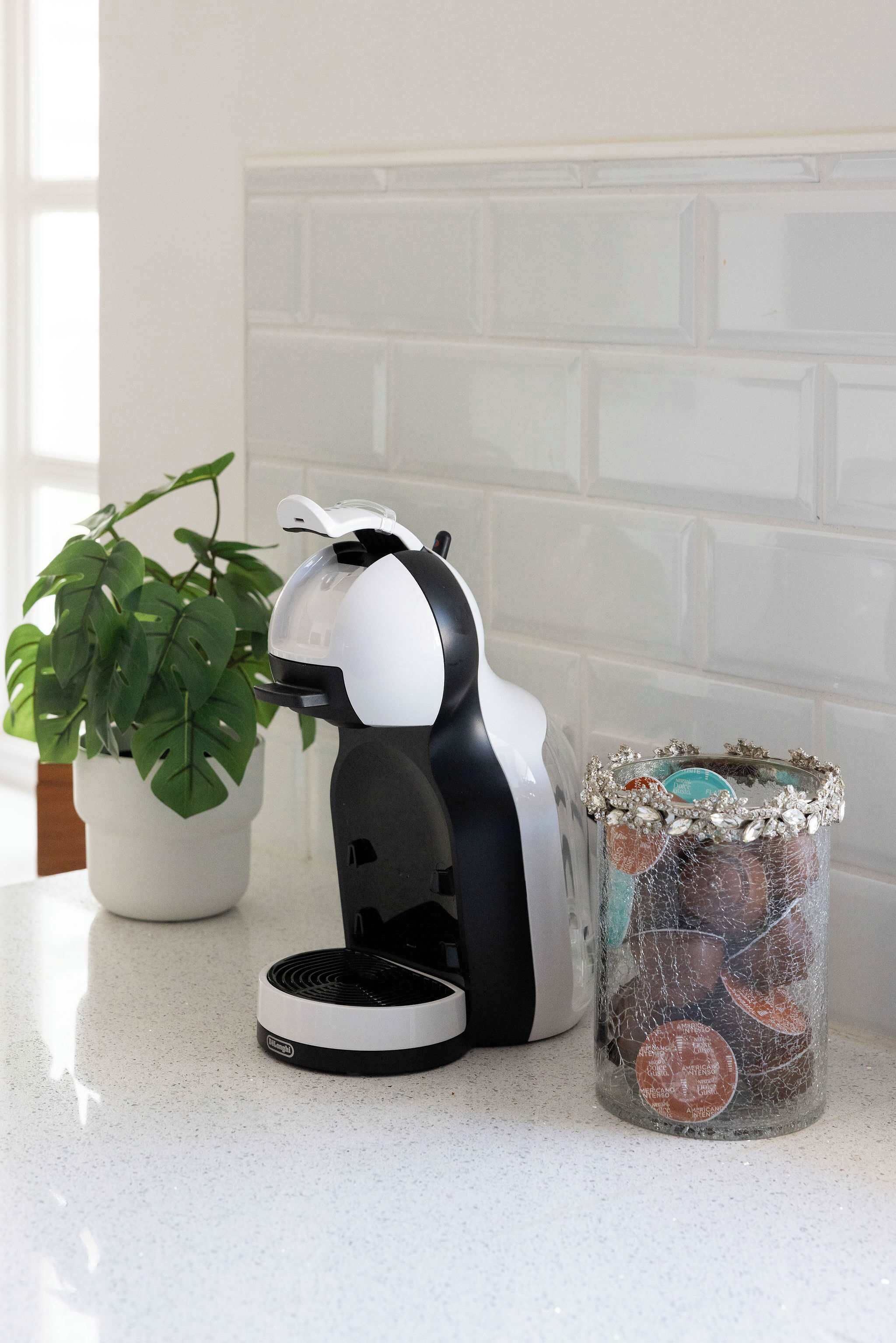 A coffee maker on a countertop next to a potted plant and a glass jar with decorative items.