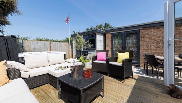 Un espace extérieur aménagé en terrasse, avec des meubles en osier, une table sur laquelle se trouvent une carafe et des verres, et un drapeau.