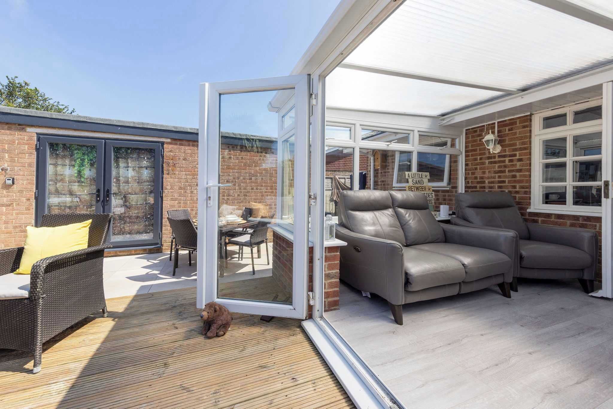 A covered patio with a glass door leading to a brick exterior, grey leather sofas, and a wicker chair.