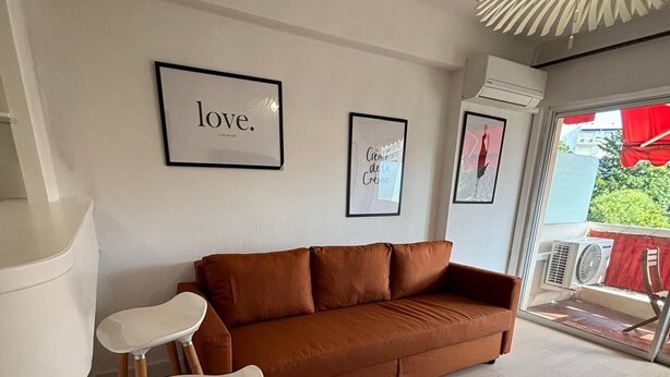 A modern living room with a brown sofa, two white chairs, and a unique ceiling light fixture. - Studio Croisette 3 mint on foot, comfortable and relaxing. (Cannes)