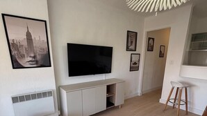 A modern living room with a flat-screen TV, white furniture, and a unique ceiling light fixture. - Studio Croisette 3 mint on foot, comfortable and relaxing. (Cannes)