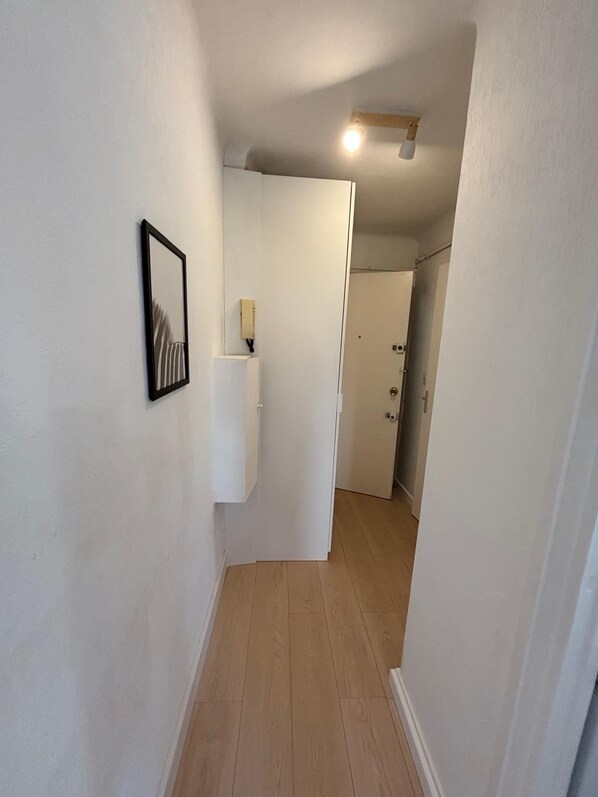 A narrow hallway with wooden flooring, white walls, and a ceiling light fixture.