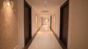 Un couloir d’hôtel avec un sol ciré, des portes sombres et un éclairage encastré.