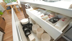 Une cuisine avec un plan de travail blanc et un organiseur de tiroir contenant des assiettes, des bols et des ustensiles de cuisine.