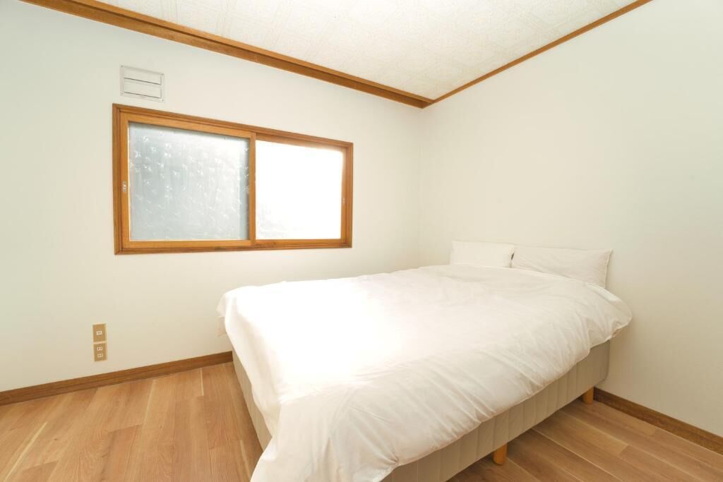 A bedroom with a single bed, a window, and wooden flooring.