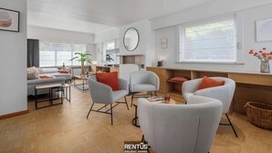 A modern living room with a sofa, armchairs, a coffee table, and a fireplace. There are large windows providing natural light and a view of the outdoors. - Coppietershof-home with garden in historic Bruges (Bruges)