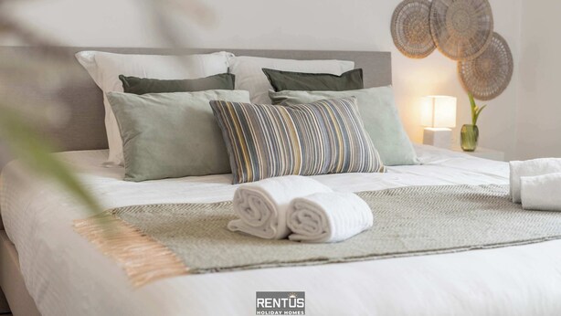 A neatly made bed with a striped pillow, a rolled towel, and a woven wall decoration. - Coppietershof-home with garden in historic Bruges (Bruges)