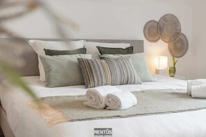 A neatly made bed with a striped pillow, a rolled towel, and a woven wall decoration. - Coppietershof-home with garden in historic Bruges (Bruges)