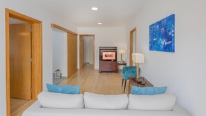 A hotel room with a wooden floor, a white sofa with blue cushions, a TV with a 'GUEST READY' sign, a blue armchair, and a blue abstract painting on the wall.