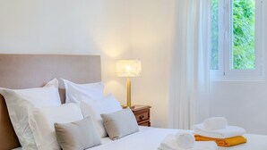 A neatly made bed with white and grey pillows, a bedside lamp, and a window with curtains.