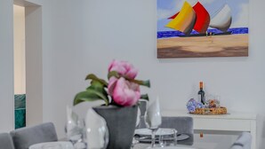 A dining area with a table set for four, a vase of pink flowers, and a painting of a sailboat on the wall.