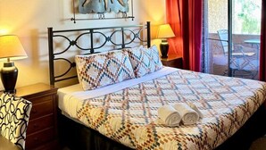 Un llit amb un estenat amb dibuixos, una obra d'art a la paret i una finestra amb cortines vermelles.