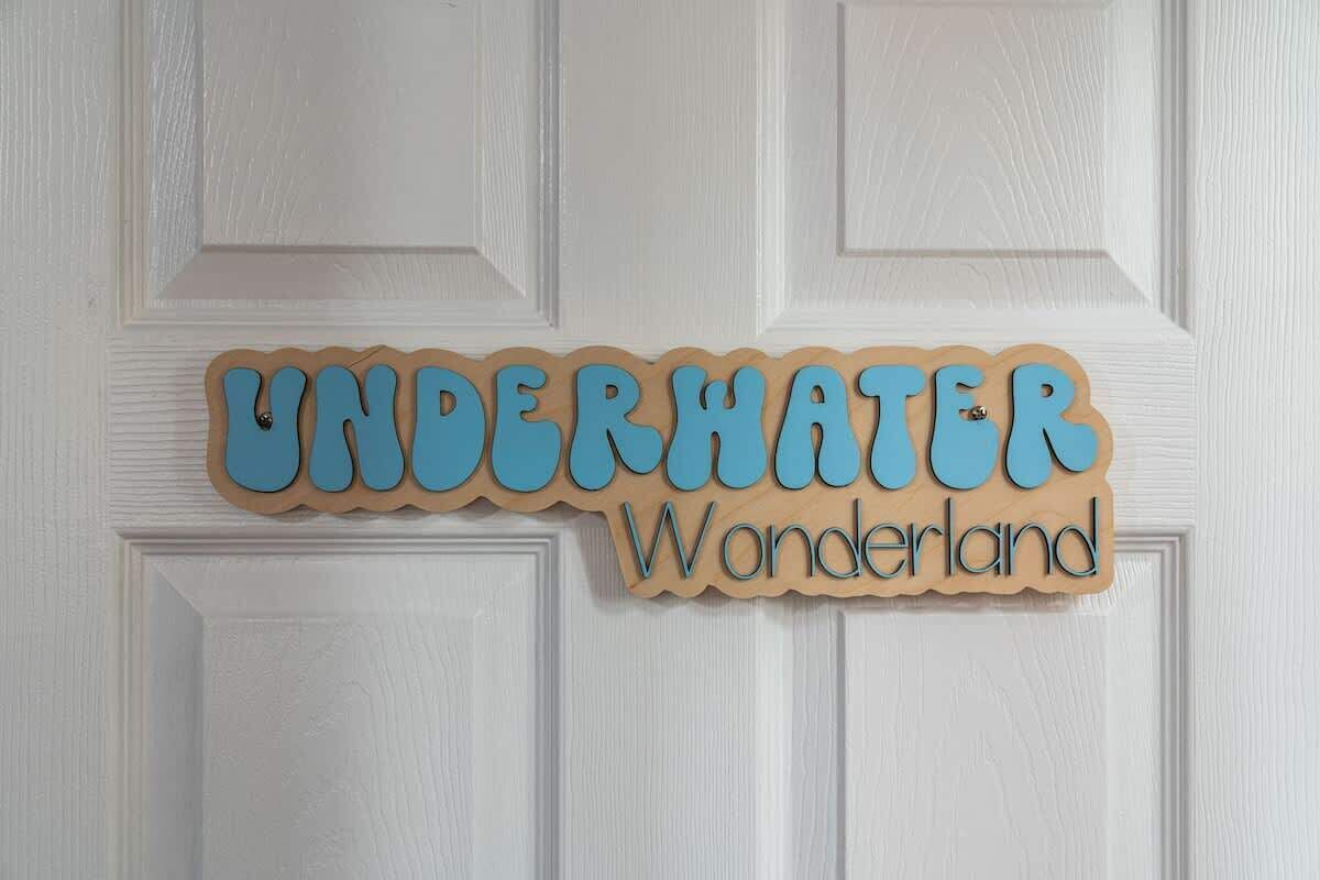 Un cartello di legno con la scritta 'UNDERHATER Wonderland' su una porta bianca.