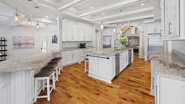 Une cuisine spacieuse avec des meubles blancs, un grand îlot central doté de tabourets et un plancher en bois.