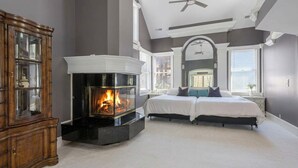 Une chambre avec une cheminée, deux lits, une armoire en bois et une fenêtre avec des stores.