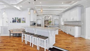 Une cuisine spacieuse avec des meubles blancs, un grand îlot central doté de tabourets, et un coin repas avec une banquette et des chaises.