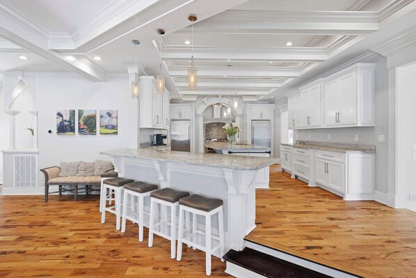 Une cuisine spacieuse avec des meubles blancs, un grand îlot central doté de tabourets, et un coin repas avec une banquette et des chaises.