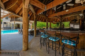An outdoor bar area with wooden beams, a pool, and a view of a house. - The Hideaway Club | Heated Pool & Game Room (McDonald)