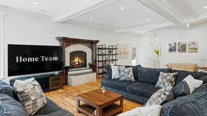 A living room with a fireplace, a large flat-screen TV, a sofa set, and a bookshelf.