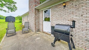 Een gevel van baksteen met een barbecue en twee stoelen op een betonnen terras.