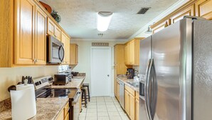 Una cocina con armarios de madera, un refrigerador de acero inoxidable, un microondas y piso de baldosas.
