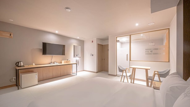 A modern hotel room with a kitchenette, a TV, a desk with chairs, and a large window. - Zzam Hotel (Jeonju)
