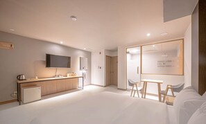 Ein modernes Hotelzimmer mit einer Küchenzeile, einem Fernseher, einem Schreibtisch mit Stühlen und einem großen Fenster.