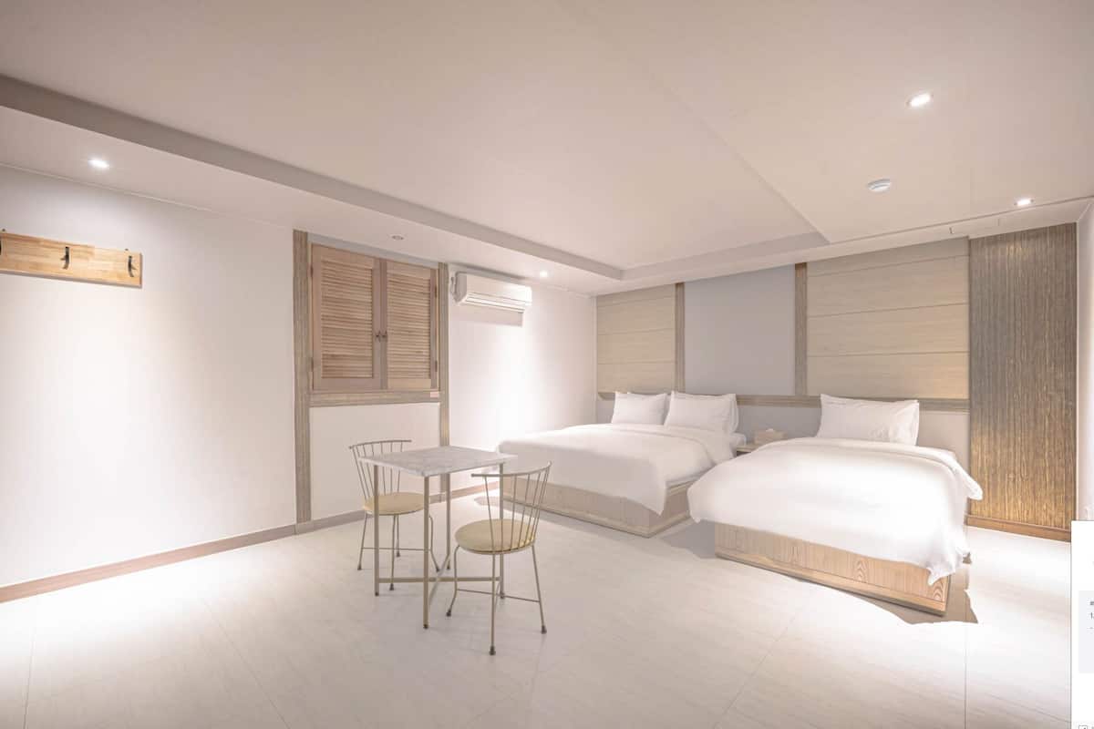 A modern hotel room with a large bed, a small table with two chairs, and a wooden wardrobe.
