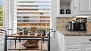 A kitchen with white cabinets, a coffee machine, and a window with blinds. - Fetch, Dine, & Unwind | Walkable Cottage Steps to North End Favs | Fun Times in Backyard! (Boise)