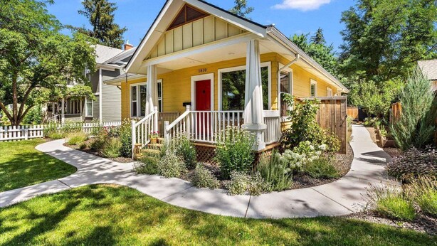 A two-story house with a yellow facade, a red door, and a white porch. - Fetch, Dine, & Unwind | Walkable Cottage Steps to North End Favs | Fun Times in Backyard! (Boise)