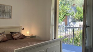 A bedroom with a bed, a nightstand, a lamp, and a view of the outside balcony.