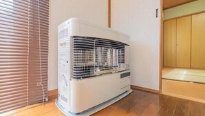 A room with a standing air conditioner, wooden flooring, a sliding door, and a small window with blinds. - UNO Toyako (Toyako)