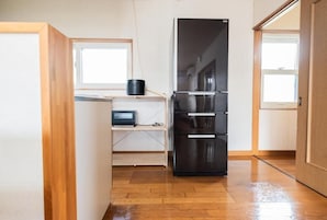 Una cocina compacta con un refrigerador negro, piso de madera y un ventanal pequeño.